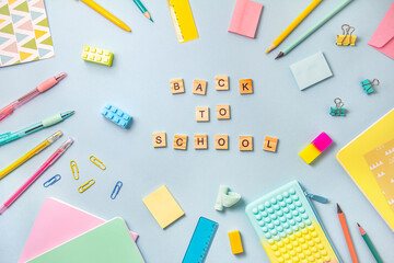 The inscription on the wooden squares in English letters is back to school. Around there are stationery in pastel colors on a blue background.