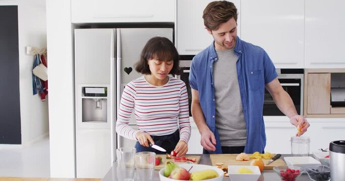 Video of happy diverse couple preparing meal together in kitchen