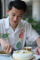 Handsome Asian young man cutting cake at afternoon tea