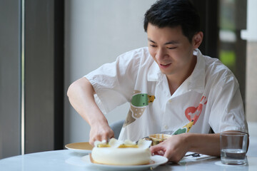 Fototapeta na wymiar smiling Asian young man cutting cake at his birthday
