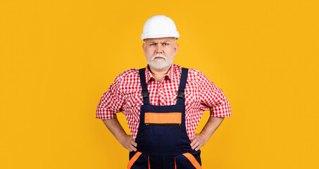 serious mature man builder in helmet on yellow background
