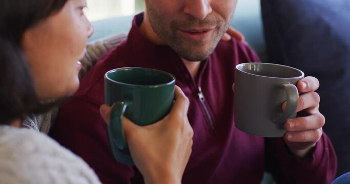 Video of back view of happy diverse couple sitting on sofa and drinking coffee