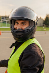 Motorcyclist in a driving lesson. Lessons in auto and motorcycle school. A student in a special uniform drives a motorcycle. Summer training on a moped. Student and teacher.	