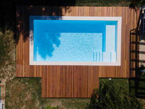 Drone flight over pool with nice wooden terrace surrounded by green lawn in beautiful garden