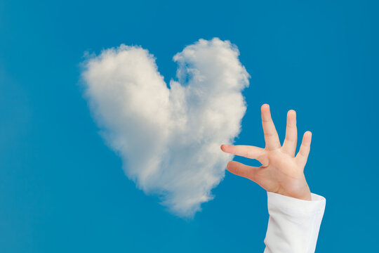 Child hand trying to hold the heart shaped cloud in the blue sky. Concept idea of inspiration, imagination, hope and dream of child.