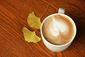 cup of coffee on wooden table and ginkgo leaf