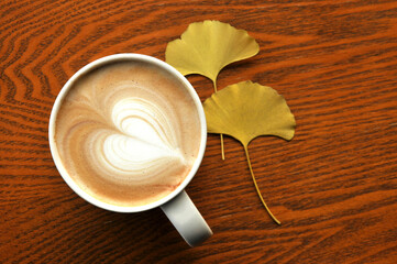 cup of coffee on wooden table and ginkgo leaf