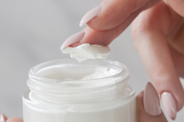 Close up of woman's hand is taking cream from a jar with her finger. Use of cosmetics with natural ingredients for clean and soft skin. Healthcare, skin care and beauty  concept.