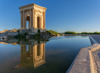 Fototapeta na wymiar Scenic panorama view of ancient water tower stone building with reflection in water pool on a blue sky summer morning at historic landmark Promenade du Peyrou garden, Montpellier, France