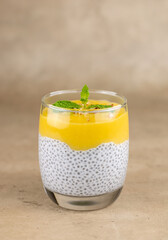 Chia seed pudding, coconut milk and mango puree in a glass cup. Close-up, on a beige background. Selective focus. Raw, vegan, sugar-free desserts.
