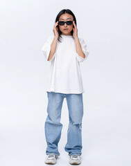 A beautiful Asian girl in a white t-shirt and blue jeans poses against a white wall in a photo studio. Fashion shooting