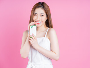 Image of young Asian woman holding milk carton on pink background