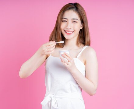 Image of young Asian woman eating yogurt on pink background