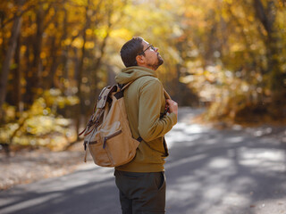 Young handsome man posing in autumn forest. young hipster guy with backpack , traveller standing in woods, Hiking, Forest, Journey, active healthy lifestyle, adventure, vacation concept.