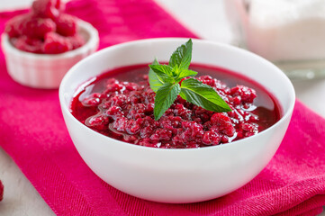 Freshly prepared raspberry jam in a white bowl on a pink napkin, close-up