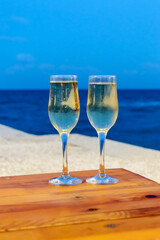 Two champagne glasses on table over sea on beach. Drink, holidays, summer vacation and celebration concept