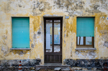 Fototapeta na wymiar La facciata di una casa abbandonata di un piccolo paese, con la porta a vetri e le finestre chiuse