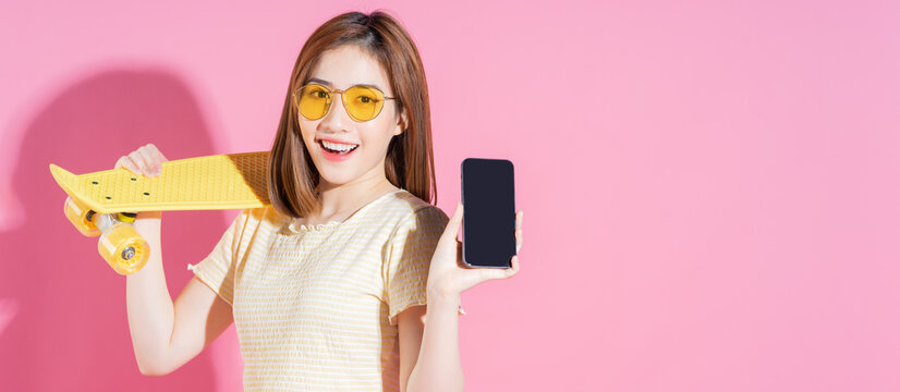 Photo of Asian teenager girl with skateboard on pink background