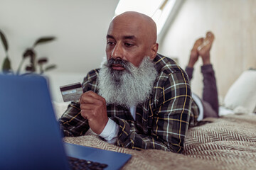 Mature man with beard and credit card shopping online at laptop