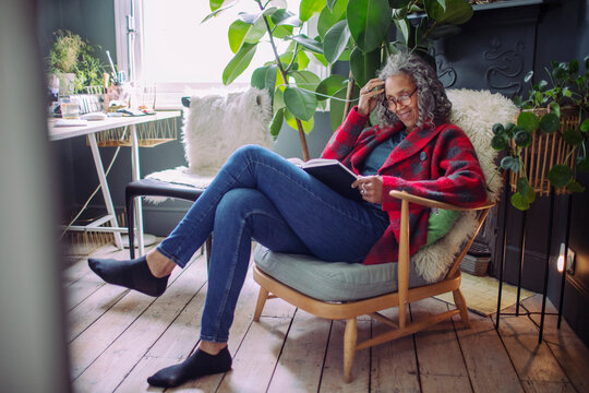 Senior woman reading book in armchair at home