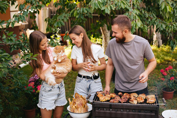 Family barbecue grill in the garden. Barbecue party. A family with a ginger cat is having fun and...