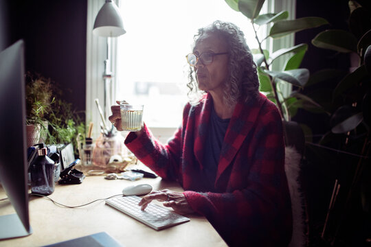 Senior woman with tea working at computer in home office