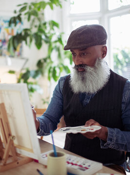 Mature man with beard and palette painting at easel