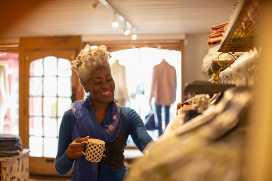 Smiling female shop owner drinking tea in clothing boutique