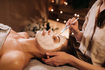 A cosmetologist makes a mask for a woman's face to rejuvenate the skin. Cosmetology