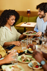 A multicultural couple is sharing food while sitting in a restaurant with their friends.