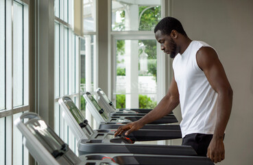 Fototapeta premium Young short curly black hair man with moustache and beard selecting running program on treadmill in the gym.