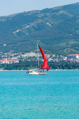 Pleasure yacht under red prause (Scarlet sails) sails along Gelendzhik Bay. Sea water sparkles in rays of sun at dawn. Beautiful seascape. Gelendzhik, Russia - July 04, 2022