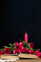 Book, tulips red candle and knitted napkin on dark wooden table