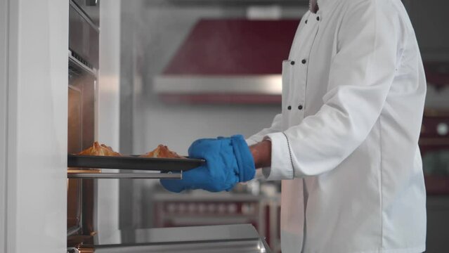 Side view of chef take tray with croissants from oven in professional kitchen. Realtime