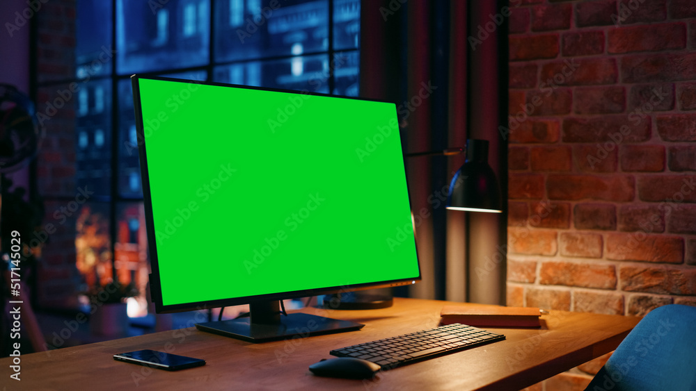 Aufkleber Desktop Computer Monitor Standing on a Table with a Green Screen Chromakey Mock Up Display. Cozy Empty Loft Apartment with Big Window with a Lamp, Notebook and Smartphone on the Table.