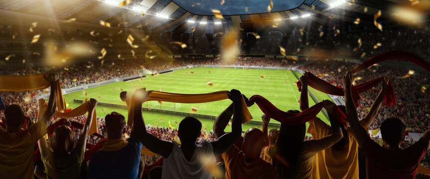 Back view of football, soccer fans cheering their team with colorful scarfs at crowded stadium at evening time. Concept of sport, support, competition. Out of focus effect