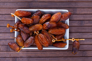 Natural dried fruits of date palm in bowl on wooden surface. Healthy superfood