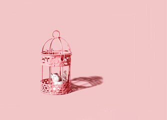 Cupid figure seating in closed bird cage. Pastel pink background. Marital customs and laws idea.