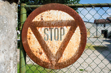 Un vecchio cartello arruginito di stop appeso ad un cancello