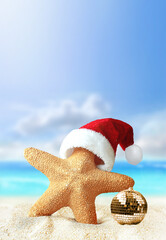Starfish in Santa Claus hat and christmas ball on a summer beach. Merry Christmas