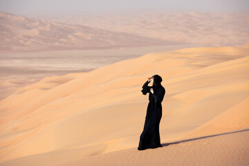 Young woman in a traditional emirati abaya in the desert. Liwa desert, Abu Dhabi, UAE.
