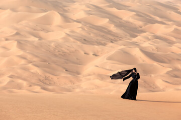 Young woman in a traditional emirati abaya in the desert. Liwa desert, Abu Dhabi, UAE. - 517150040