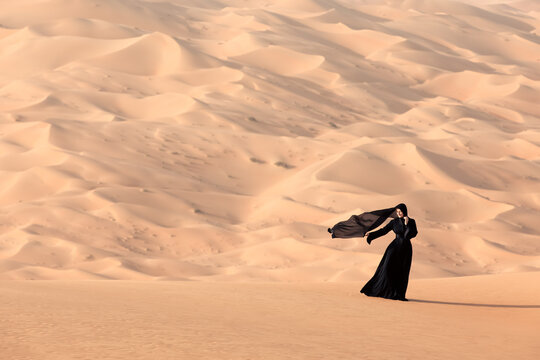 Young woman in a traditional emirati abaya in the desert. Liwa desert, Abu Dhabi, UAE.