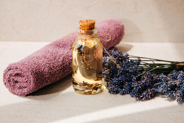 Lavender oil on light stone background with violet towel and lavender flowers. Front view