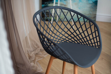 Stylish black mesh chair with wooden legs on the background of the apartment