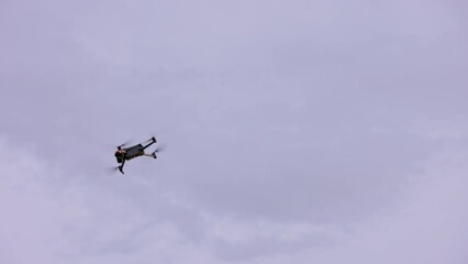 small modern civilian quadcopter drone maneuvering in cloudy sky, view from ground
