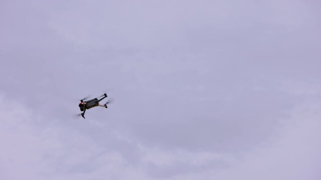 small modern civilian quadcopter drone maneuvering in cloudy sky, view from ground