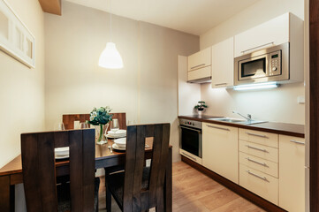 A small modern kitchen including a dining area with a table and four large comfortable chairs. The kitchen has common appliances in the form of an oven, hob and microwave.