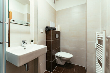 Fototapeta na wymiar A small modern bathroom with a large square sink and toilet. The tiling in the bathroom is two-tone, consisting of brown and beige tiles. There are also some additional items as towel, candles, etc.