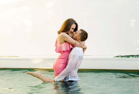 beautiful young couple in dress having fun in pool and kissing